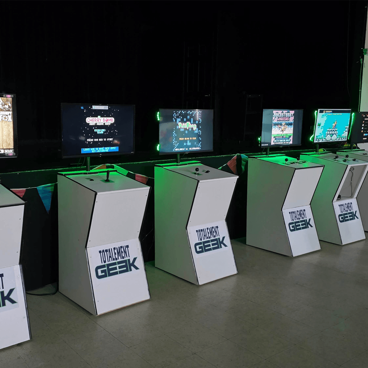 Rangée de bornes d'arcade Totalement Geek éclairées en vert dans une salle événementielle