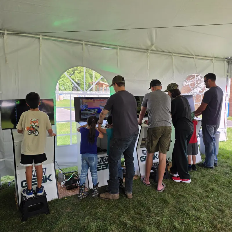 Parents et enfants jouent côte à côte aux bornes d'arcade Totalement Geek sous un chapiteau